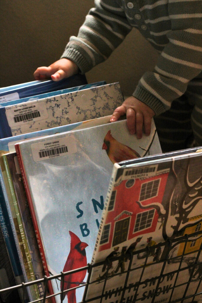 a baby's hands flipping through a basket of winter picture books